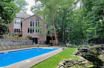 Serene backyard with a sparkling pool, lush greenery, and a tranquil pond.