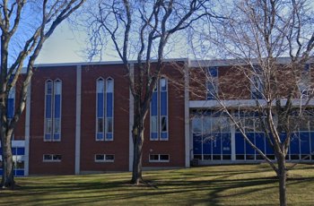 A large brick building with tall windows, surrounded by leafless trees.