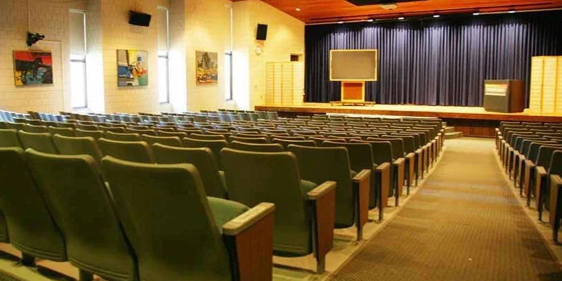 Empty auditorium with green seats facing stage and podium