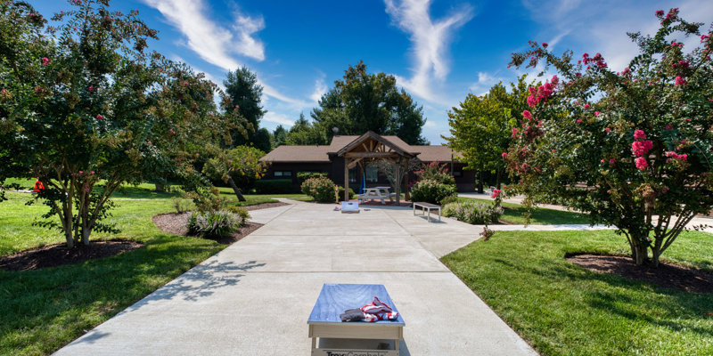 Outdoor garden with trees, cornhole games, and a walkway.