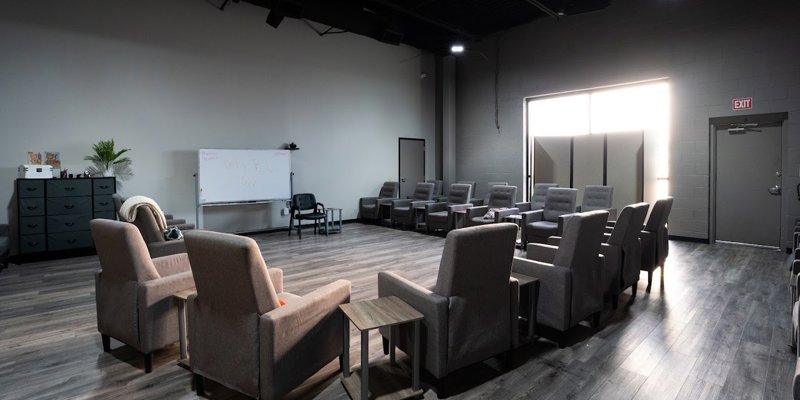 A spacious group therapy room with gray chairs and a whiteboard.