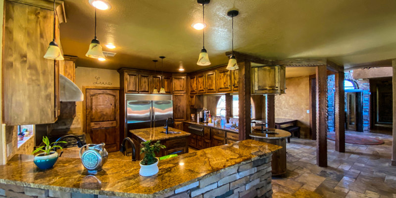 Warm-toned kitchen with stone-faced counters, wood cabinetry, pendant lighting, and stainless steel appliances