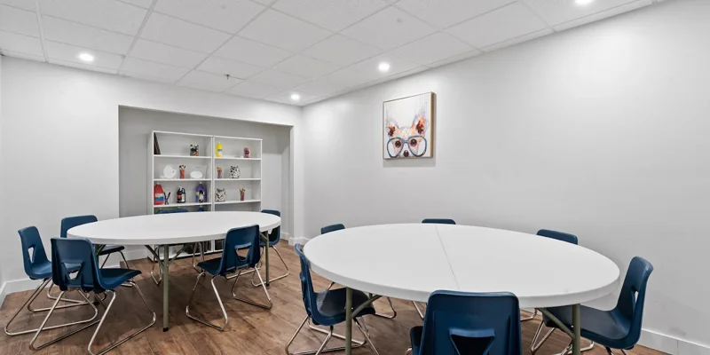 Art therapy space with white walls, round tables, blue chairs, and creative supplies