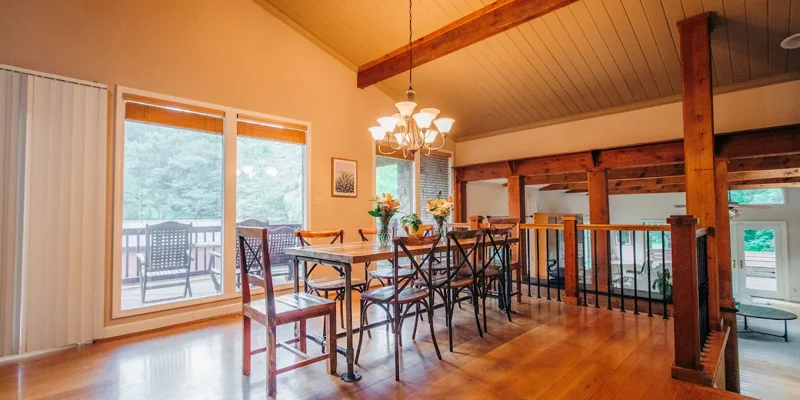 Wooden dining table with chairs under a chandelier near large windows and balcony access