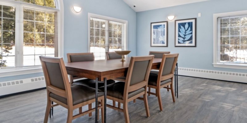 Dining area with chairs at a table and large windows.