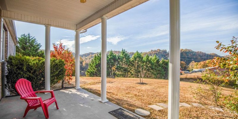 Covered porch with red chair overlooking grassy yard and trees