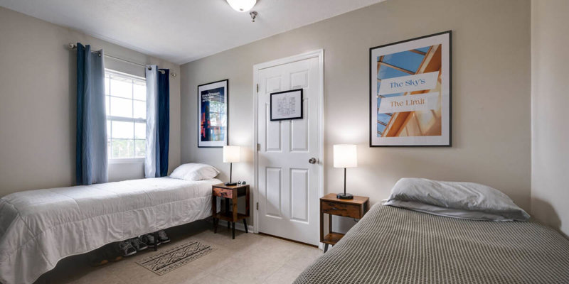 Twin bedroom with a window, blue curtains, and framed wall art.