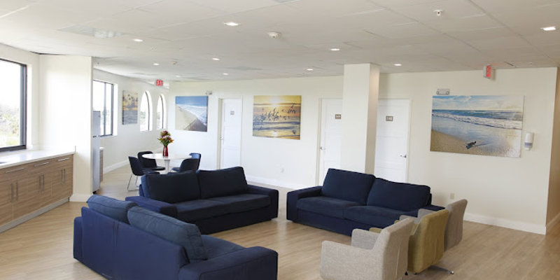 Lounge area with blue couches, white walls, and beach-themed artwork.