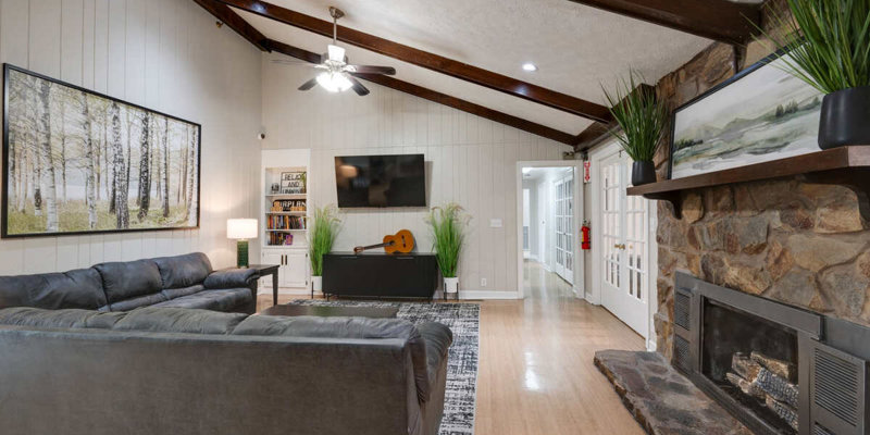 Cozy lounge with a fireplace, TV, guitar, and dark gray sofas.