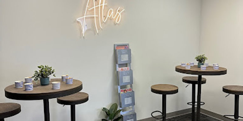 A social lounge with high-top tables, stools, and a neon "Atlas" sign.