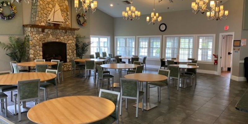 A dining hall with round tables, chandeliers, and a stone fireplace.