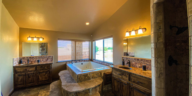 Spacious bathroom featuring a stone step-up tub, double vanities, mirrors, and warm lighting