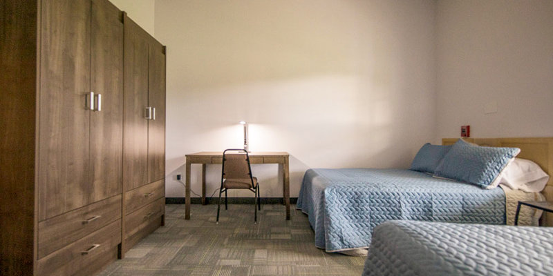 A bedroom with two beds, a desk, and a large wooden wardrobe.