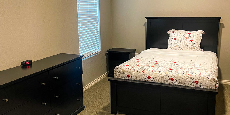 Private bedroom with a bed, dresser and a window.