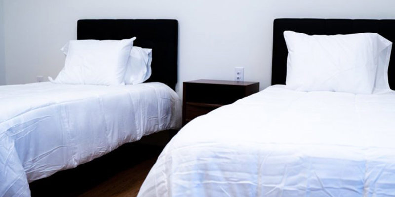 A bedroom with two beds, white bedding, and a nightstand
