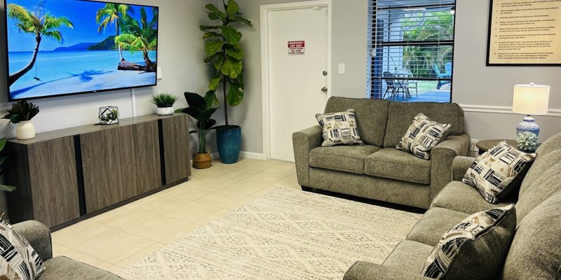 Common area with gray sofas, a large TV, and decorative pillows.