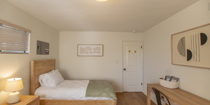 A private bedroom with a wooden bed, desk, and neutral decor.