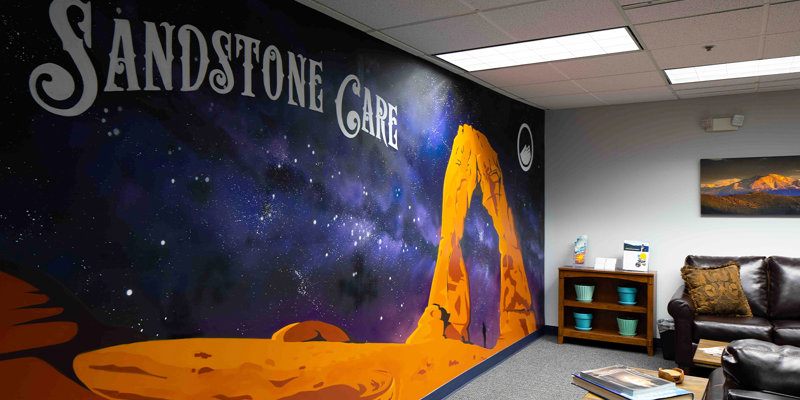 A waiting area with a mural reading "Sandstone Care" and a leather couch.