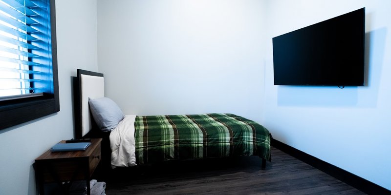 Simple rehab bedroom with a single bed, TV, and wood flooring.