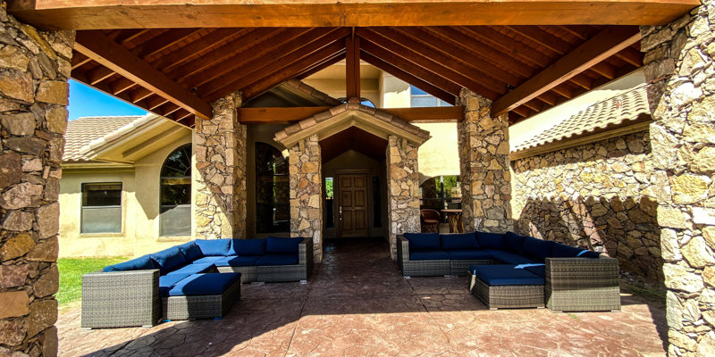 Covered patio with stone columns, exposed wooden beams, and modern cushioned seating arranged for conversation