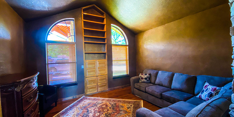 Cozy indoor room with arched windows, built-in shelving, a large sectional sofa, wooden flooring, and a decorative rug