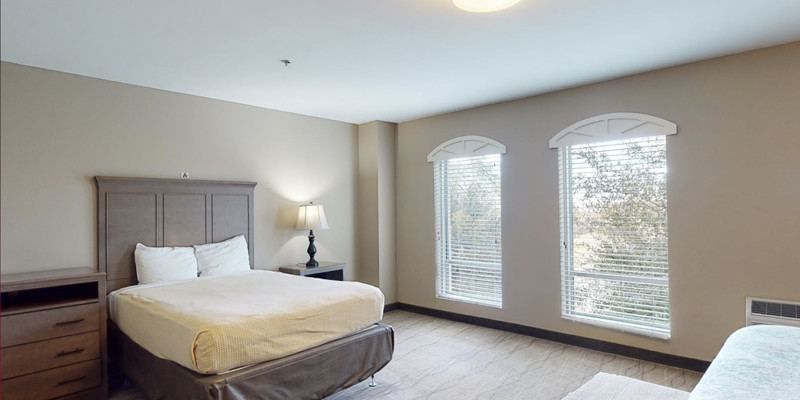 A spacious bedroom with a queen bed and large windows.