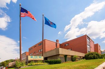 A wide view of AdCare Hospital with flags and a blue sky.
