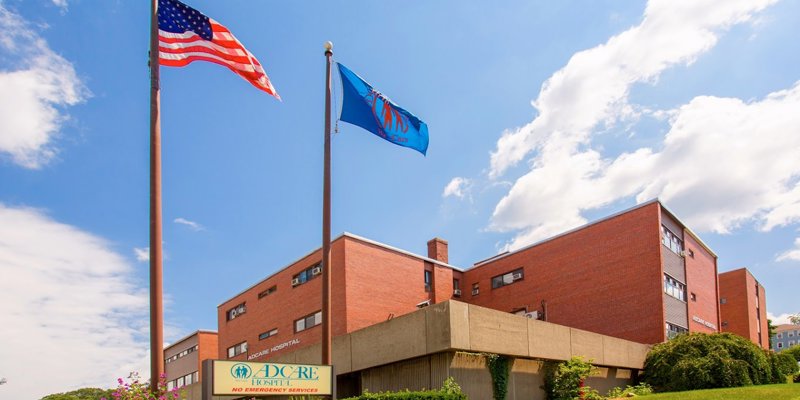 A wide view of AdCare Hospital with flags and a blue sky.