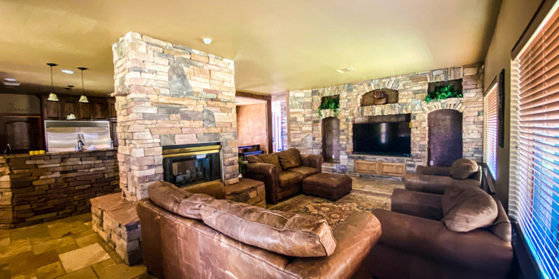 Inviting living room with multiple seating areas, stone fireplace, large TV, and rustic interior details
