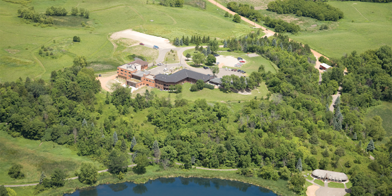 Aerial view of rehab facility surrounded by greenery next to a lake.