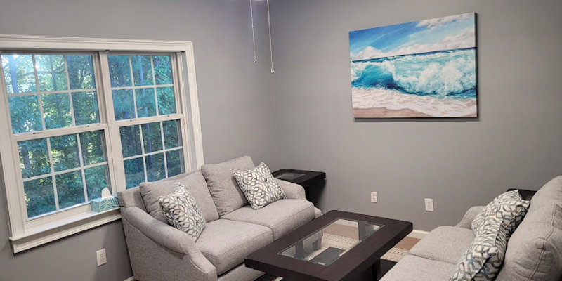 A cozy lounge with gray sofas, a glass coffee table, and ocean artwork.