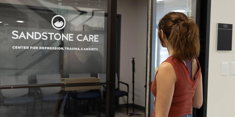 A woman standing outside Sandstone Care’s glass entrance.